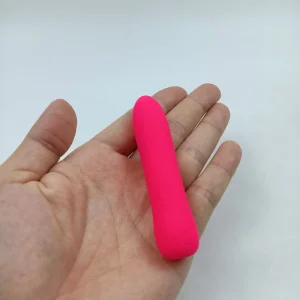 Watermelon red mini silicone vibrating bullet resting flat on an open palm to demonstrate size